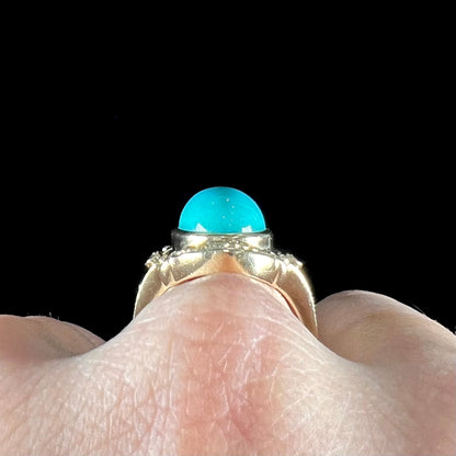 A yellow gold ring set with a greenish blue Sleeping Beauty turquoise cabochon with two diamond accents.