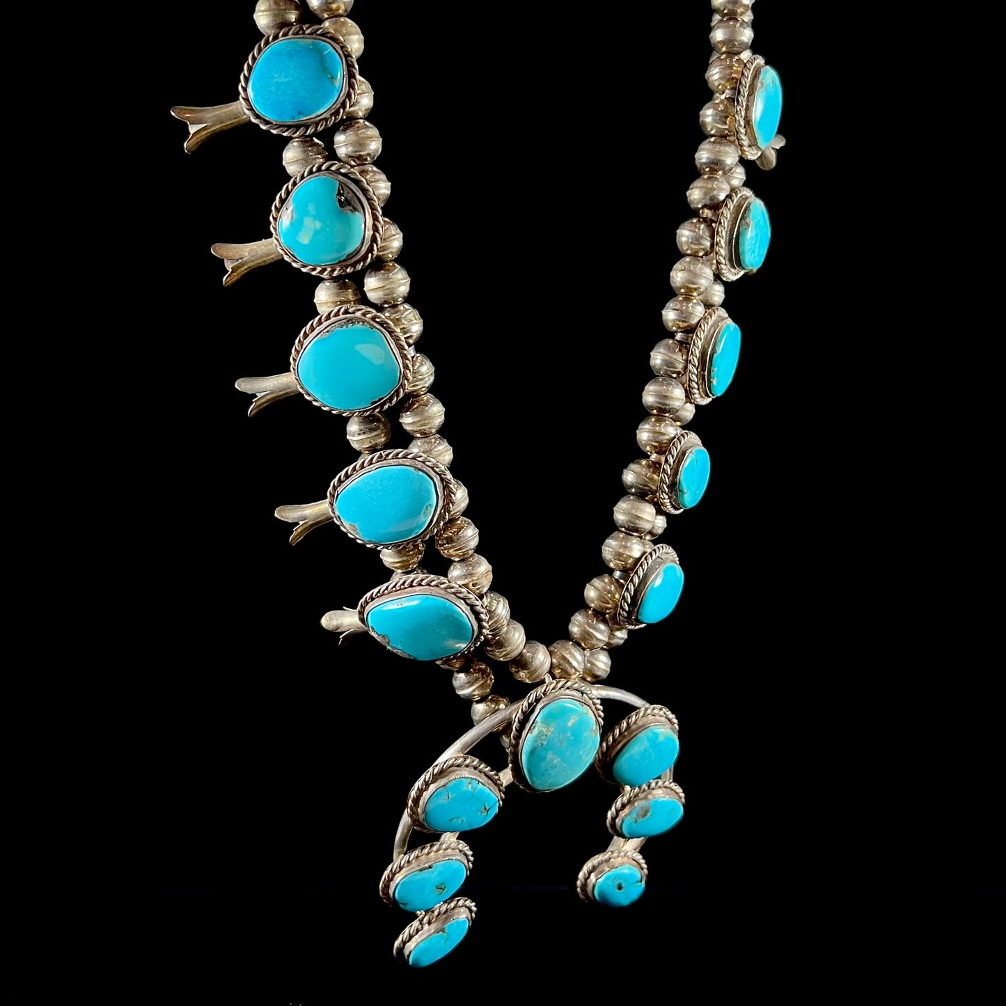 A sterling silver, Navajo style squash blossom necklace set with Morenci turquoise stones.  The legnth is designed for women and children.