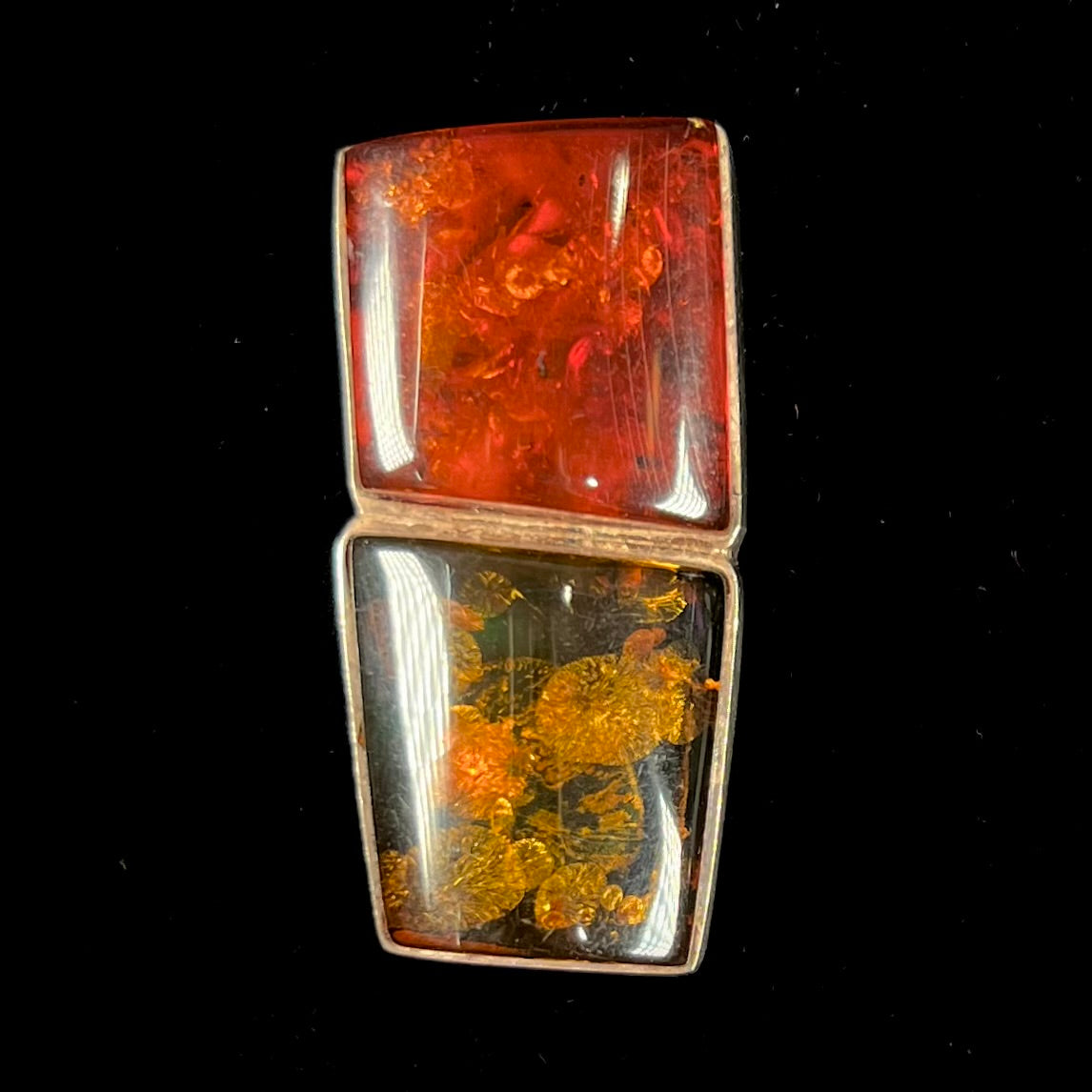 A sterling silver pendant brooch set with a red orange amber and a yellow sun-spangled amber.