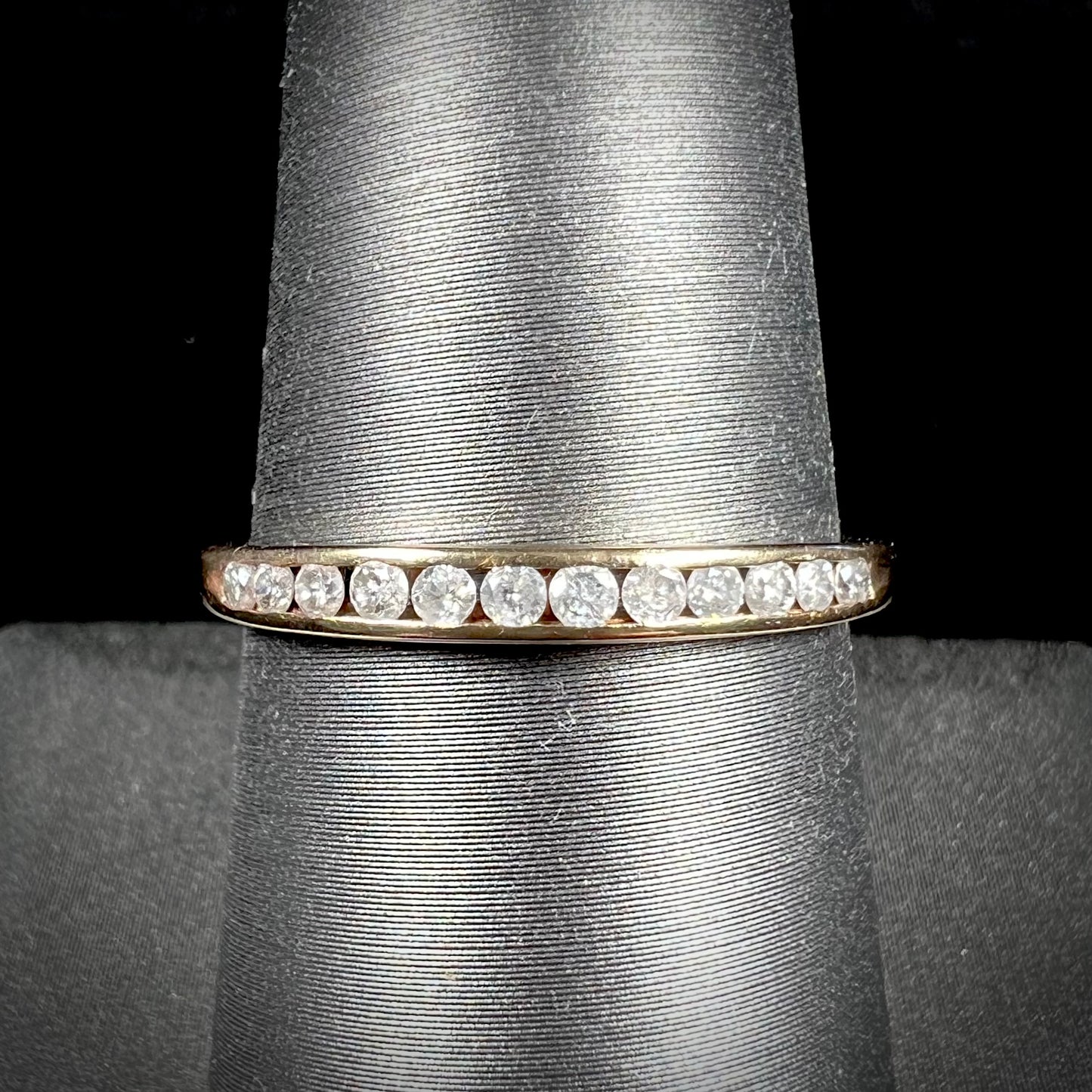 A unisex, thin yellow gold wedding band channel set with 12 round cut diamonds.