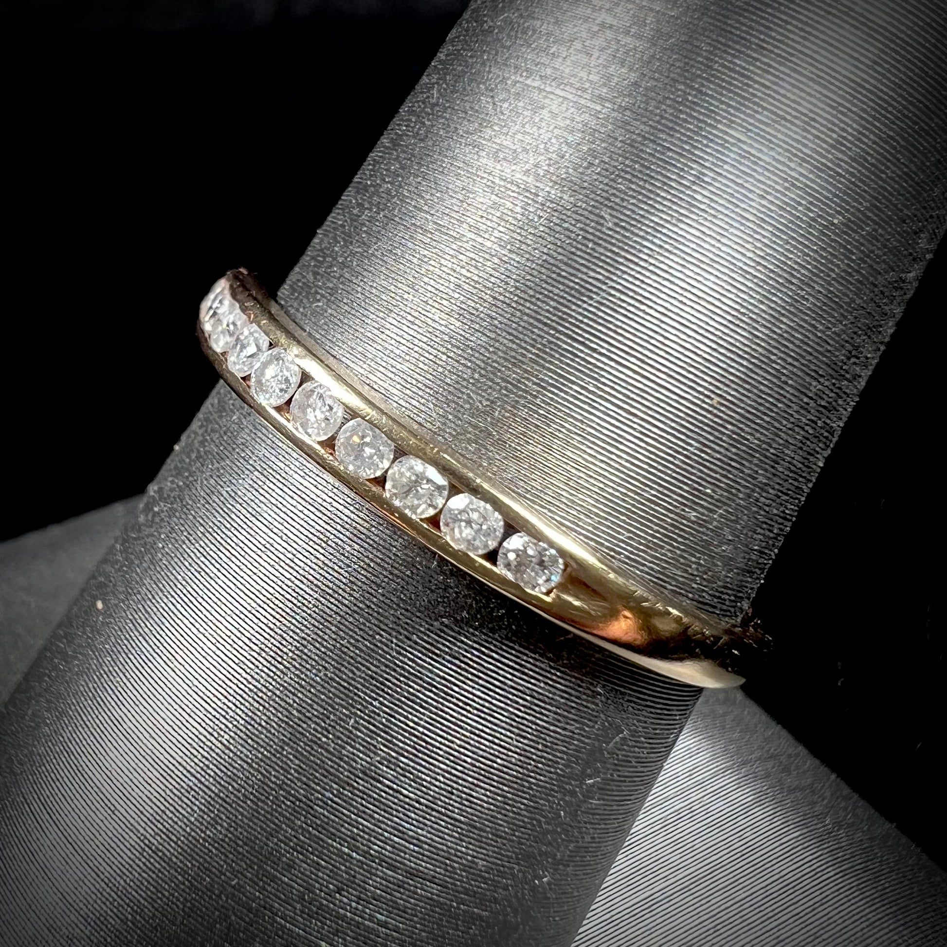 A unisex, thin yellow gold wedding band channel set with 12 round cut diamonds.