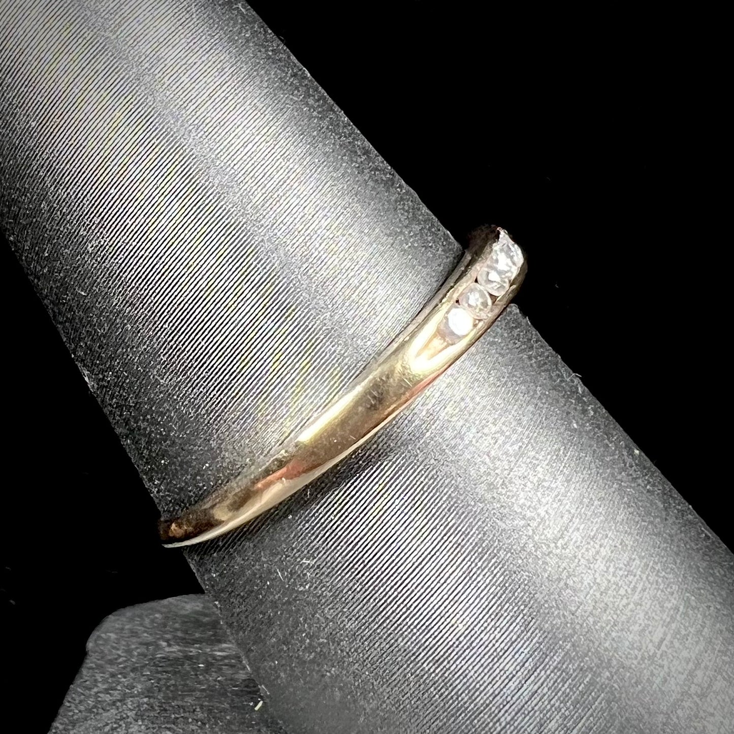 A unisex, thin yellow gold wedding band channel set with 12 round cut diamonds.