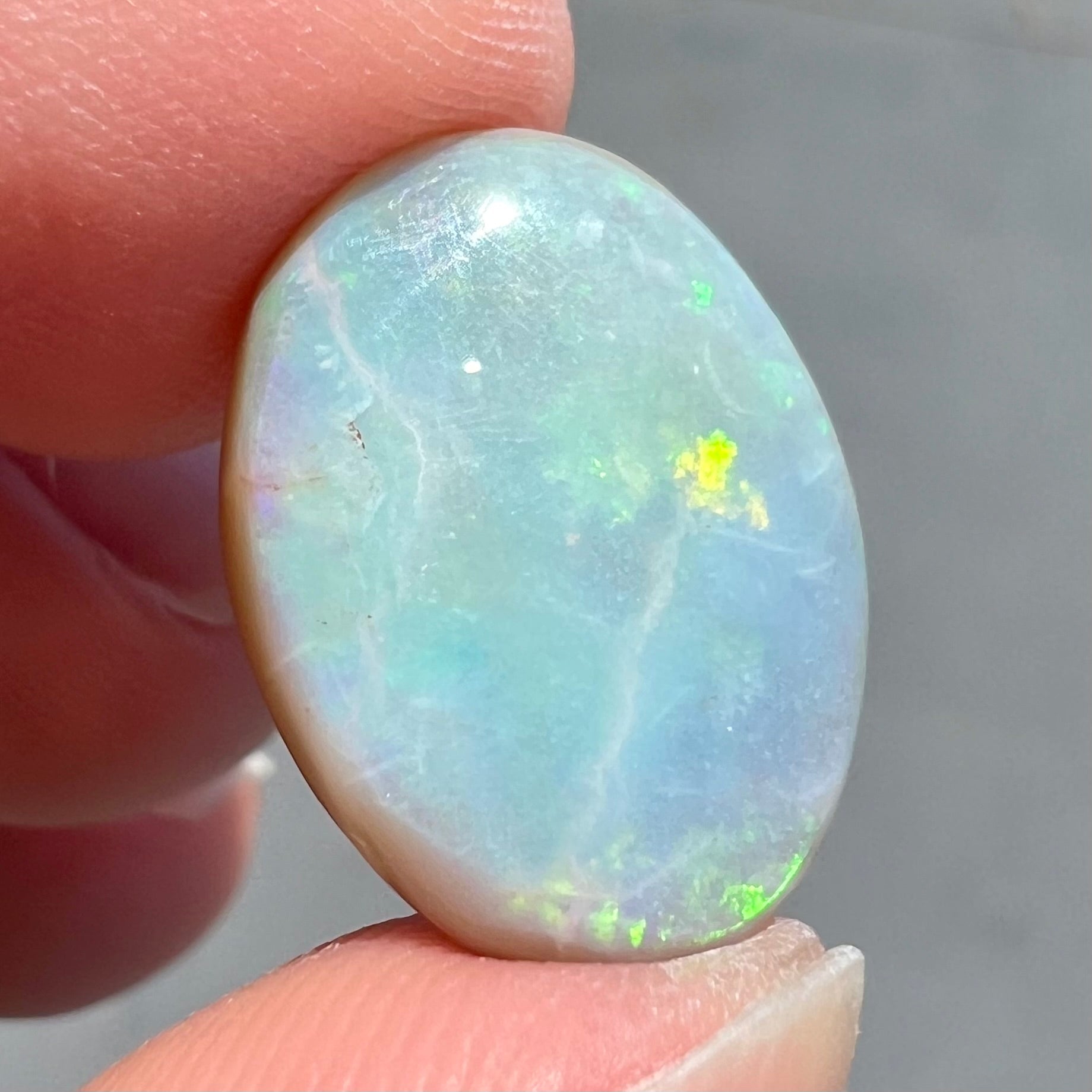 A loose, oval cut light opal stone from Mintabie, Australia.  The stone shows dull orange and green colors.