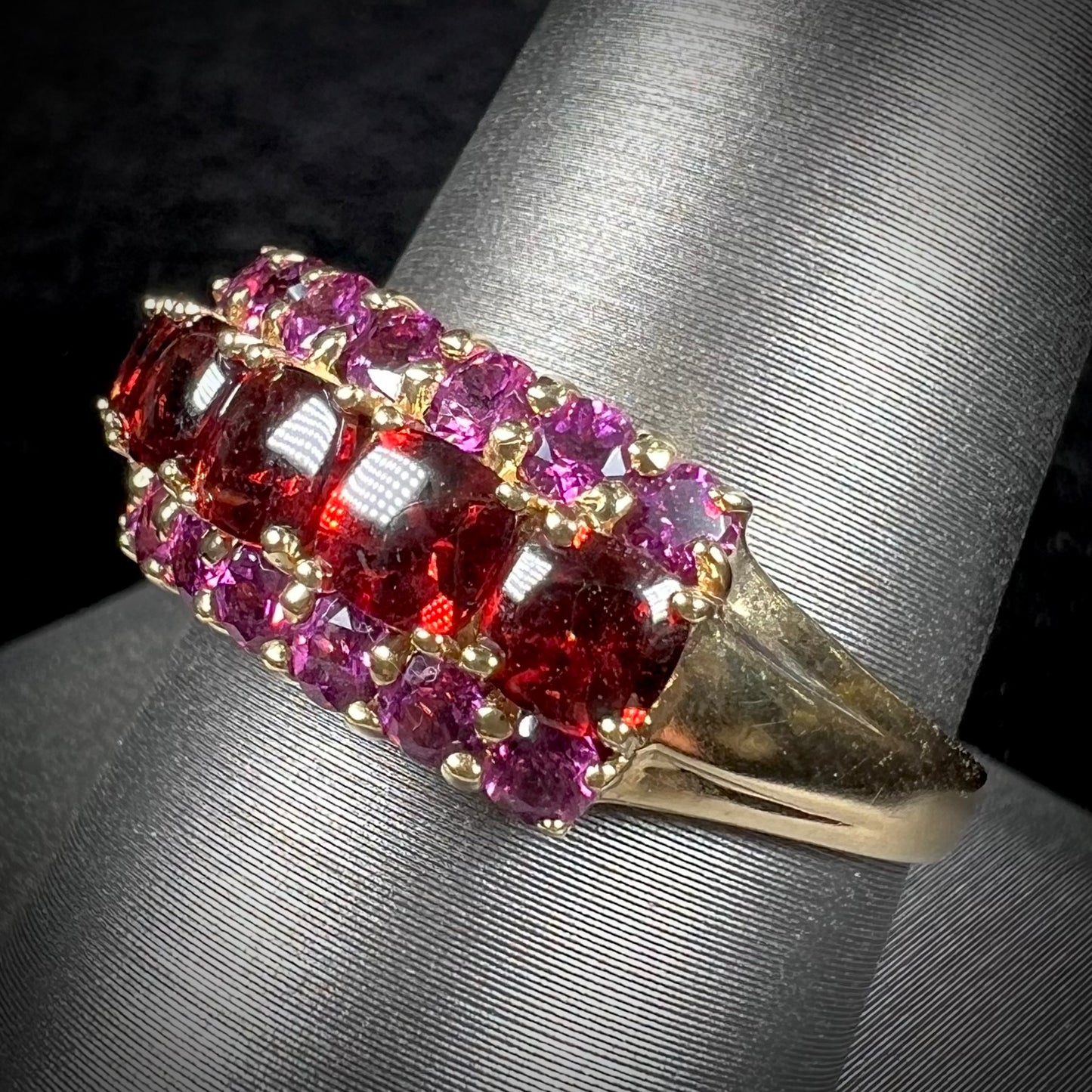 A gold ring set with buff cut cushion shaped almandine garnets with round cut purple rhodolite garnet accents.