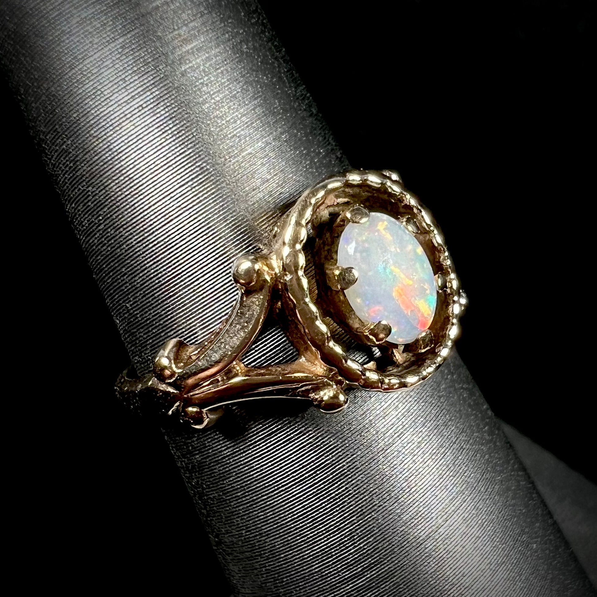 A ladies' Art Nouveau style opal solitaire ring.  The mounting is yellow gold with filigree accents.