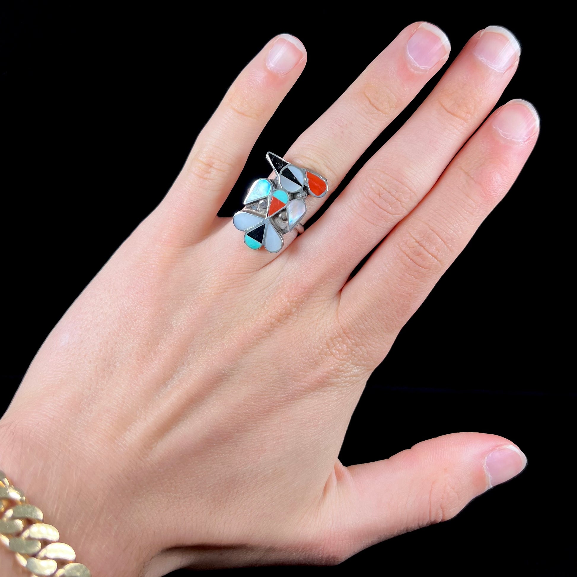 A vintage, sterling silver Zuni thunderbird ring inlaid with turquoise, mother of pearl, onyx, and coral stones.