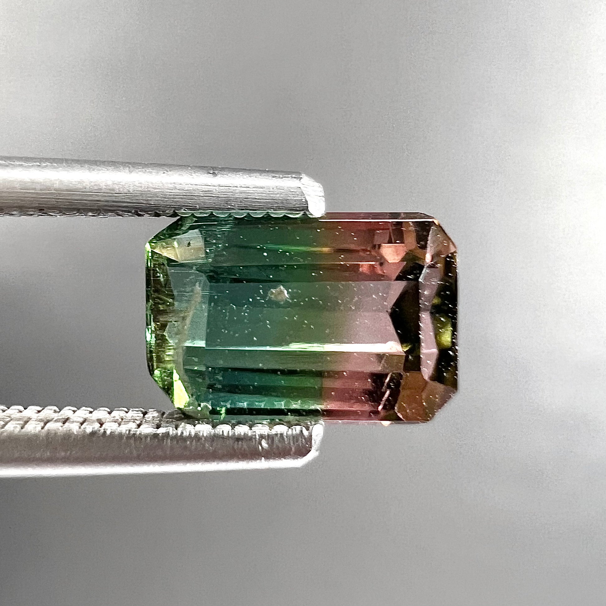 A loose, emerald cut tricolor watermelon tourmaline stone.  Colors displayed in the stone are green, blue, and pink.
