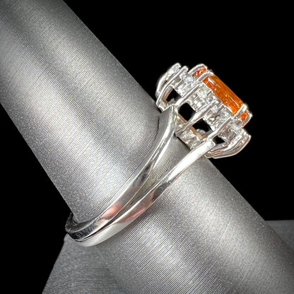A white gold split shank ring set with an oval cut orange sapphire and a halo of white sapphires.