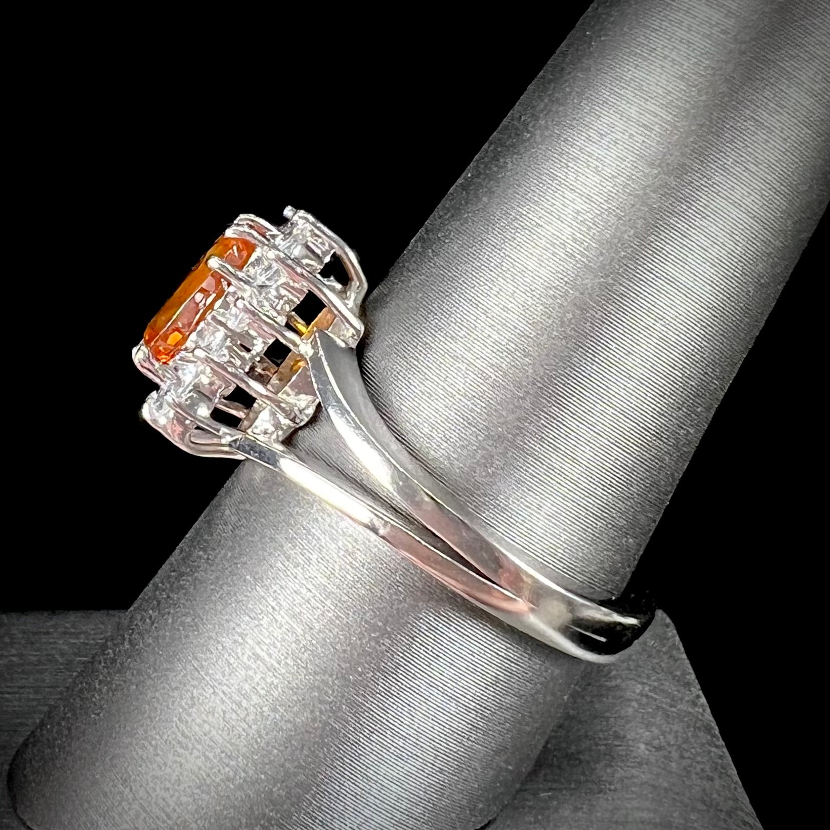 A white gold split shank ring set with an oval cut orange sapphire and a halo of white sapphires.