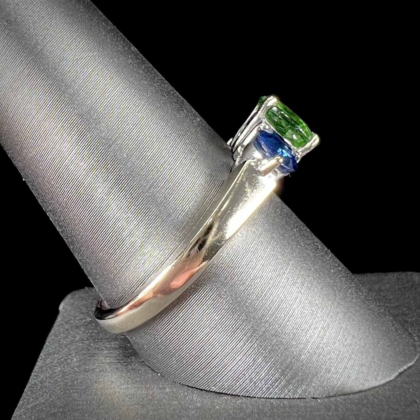 A ladies' white gold three stone ring set with two round blue sapphires and an oval cut green tsavorite garnet.