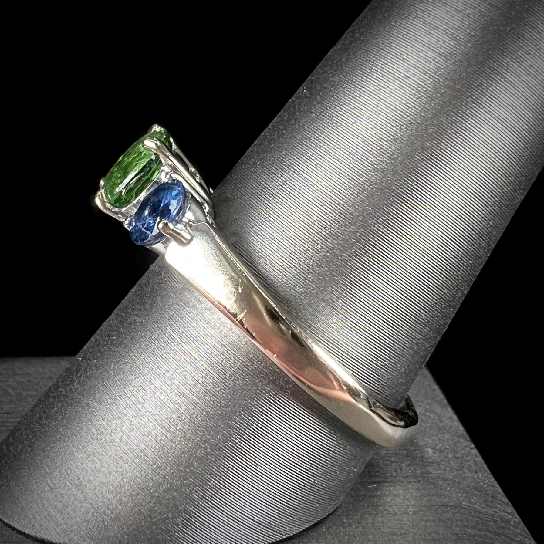 A ladies' white gold three stone ring set with two round blue sapphires and an oval cut green tsavorite garnet.