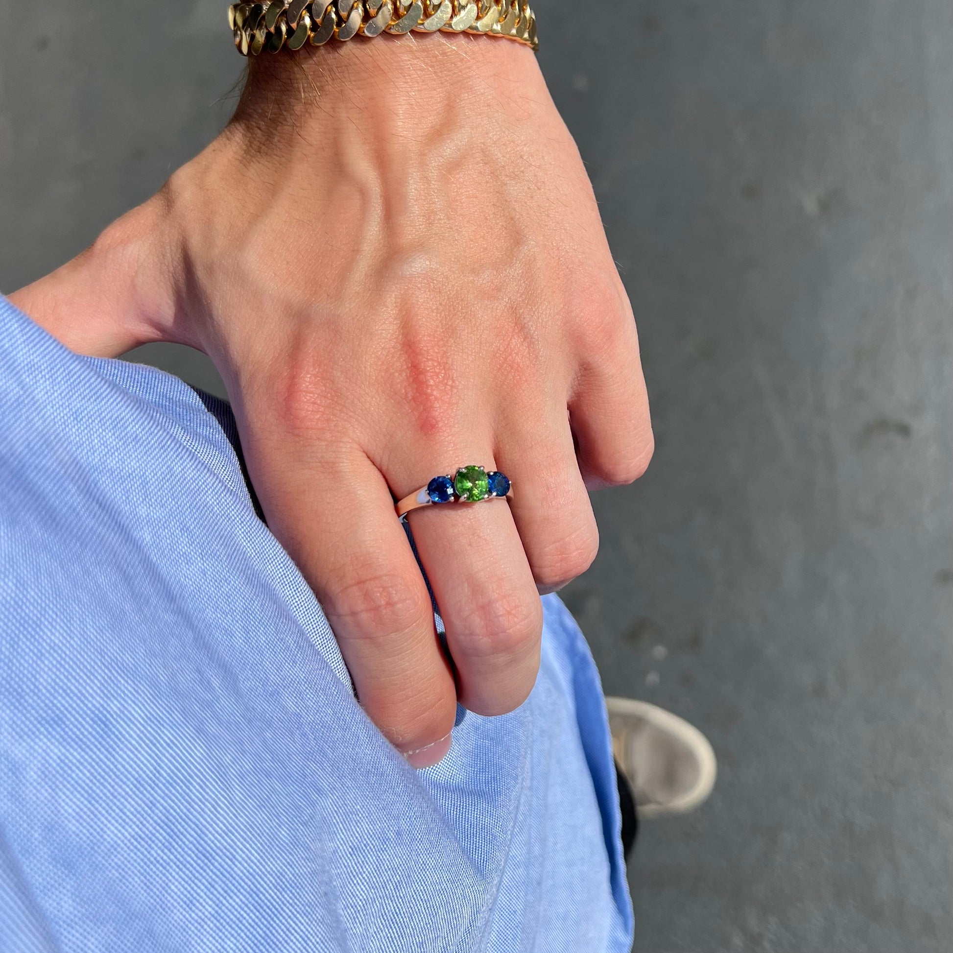 A ladies' white gold three stone ring set with two round blue sapphires and an oval cut green tsavorite garnet.