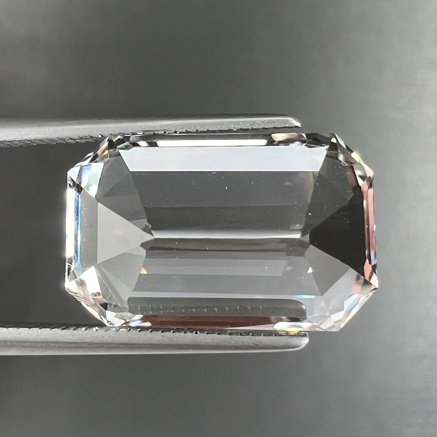 A loose, emerald cut topaz gemstone from Russia.  The stone is a faint pinkish white color.