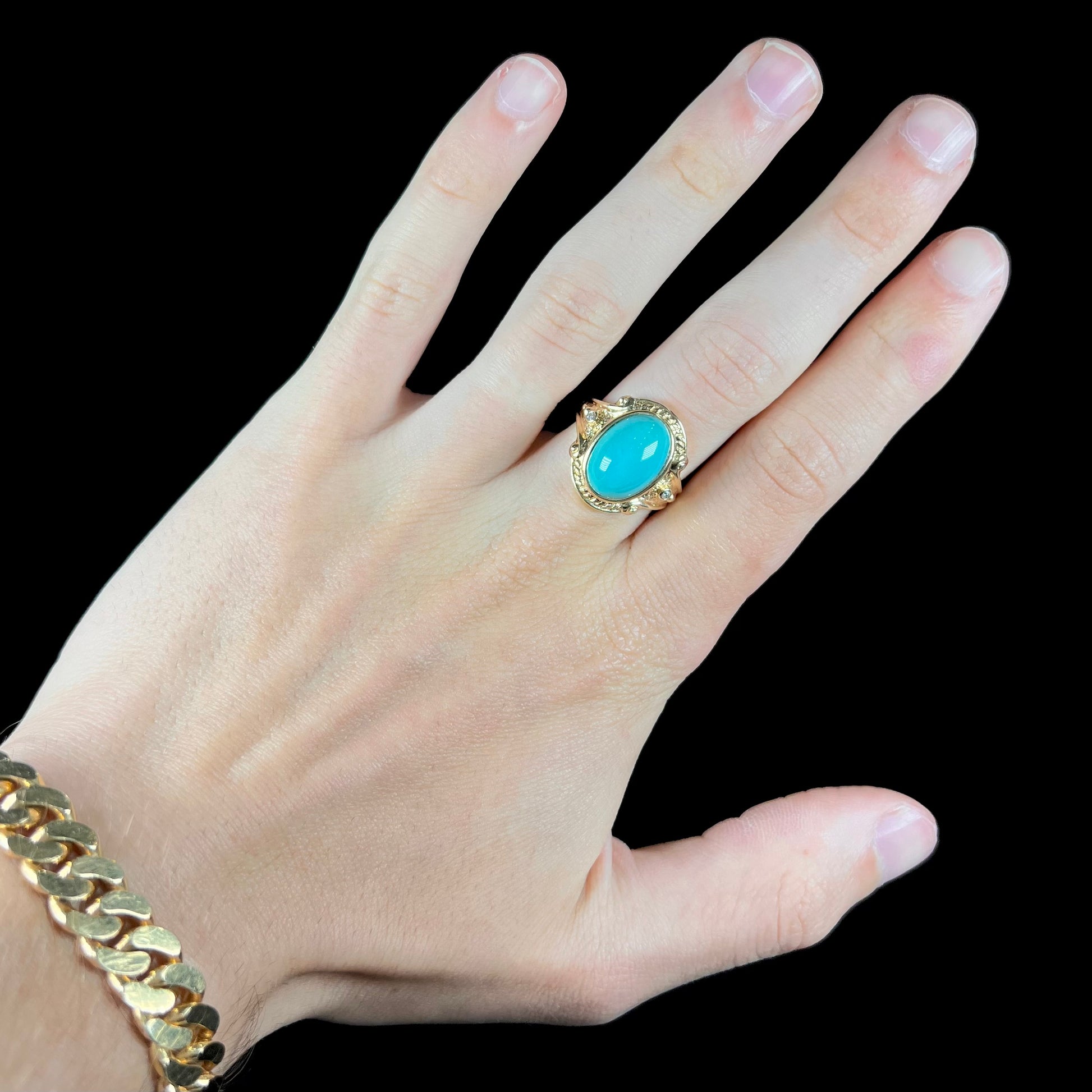 A yellow gold ring set with a greenish blue Sleeping Beauty turquoise cabochon with two diamond accents.