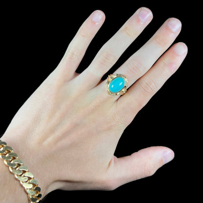 A yellow gold ring set with a greenish blue Sleeping Beauty turquoise cabochon with two diamond accents.