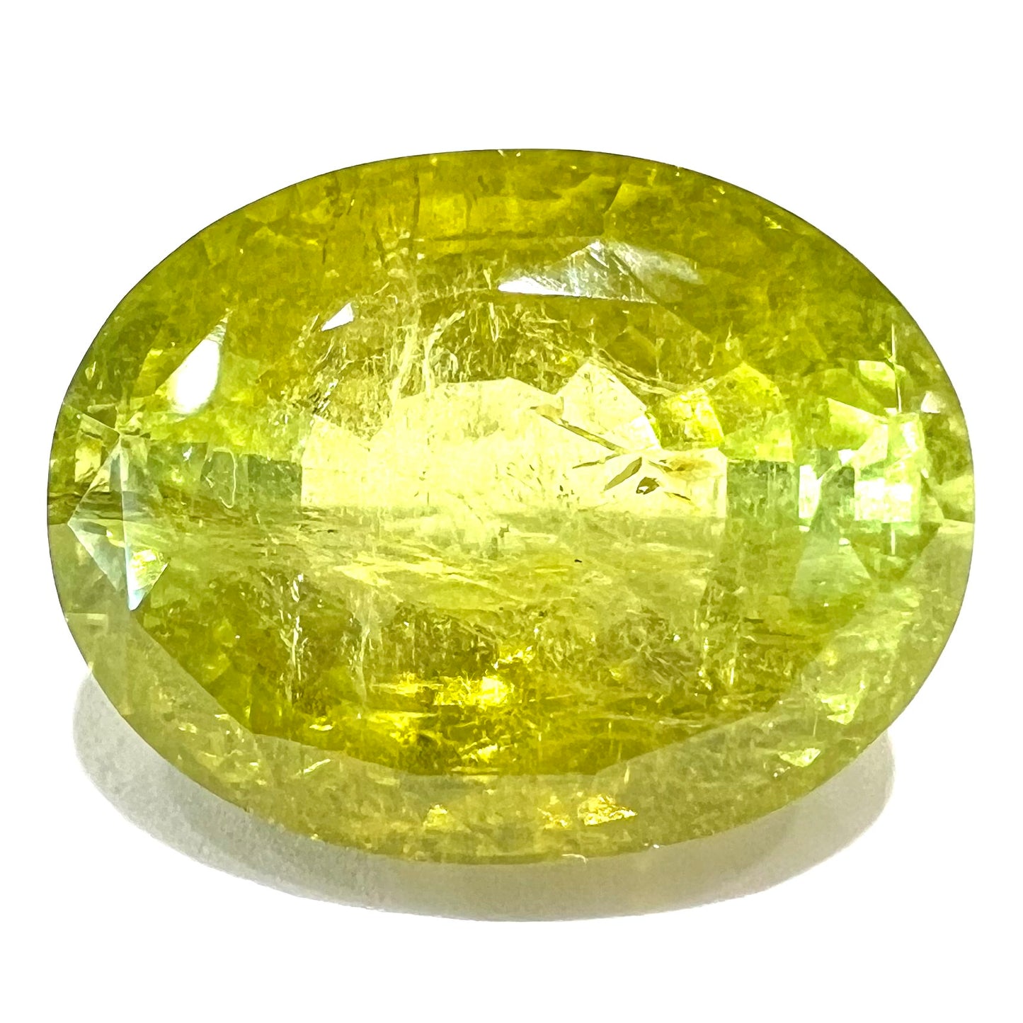 A loose, faceted oval cut green tourmaline stone.  The color is an almost neon yellow-green.