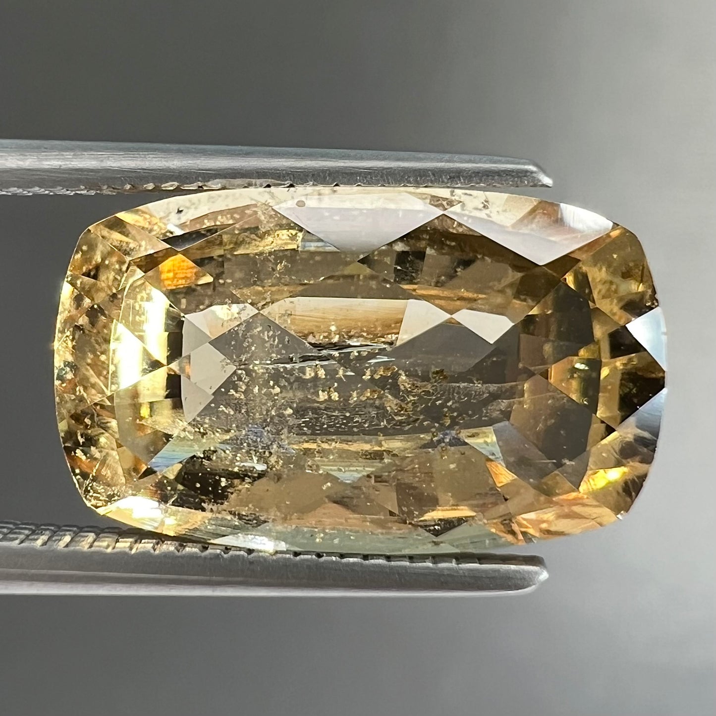 A loose, checkerboard cushion cut golden topaz gemstone.  The stone is a yellow color.