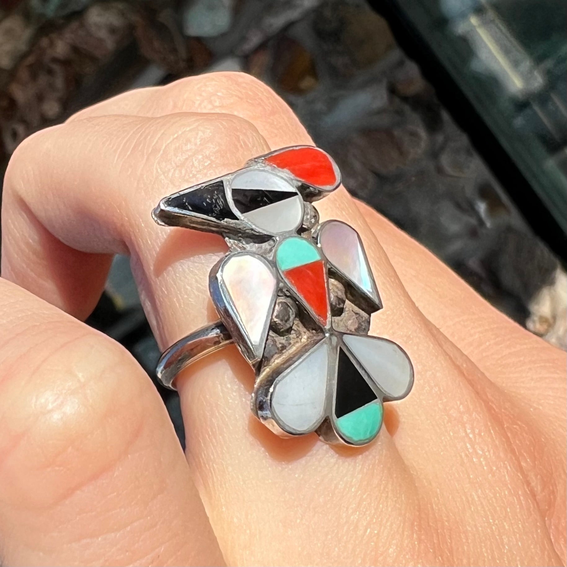 A vintage, sterling silver Zuni thunderbird ring inlaid with turquoise, mother of pearl, onyx, and coral stones.