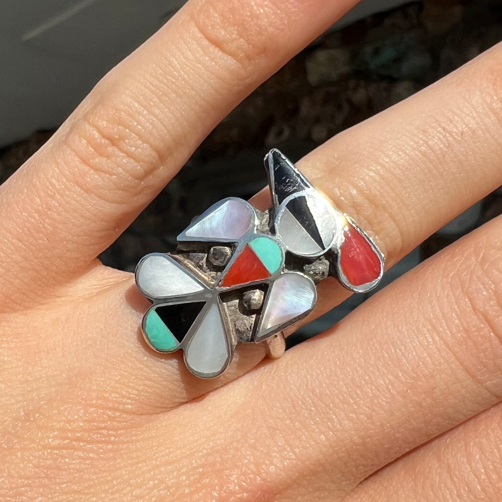 A vintage, sterling silver Zuni thunderbird ring inlaid with turquoise, mother of pearl, onyx, and coral stones.