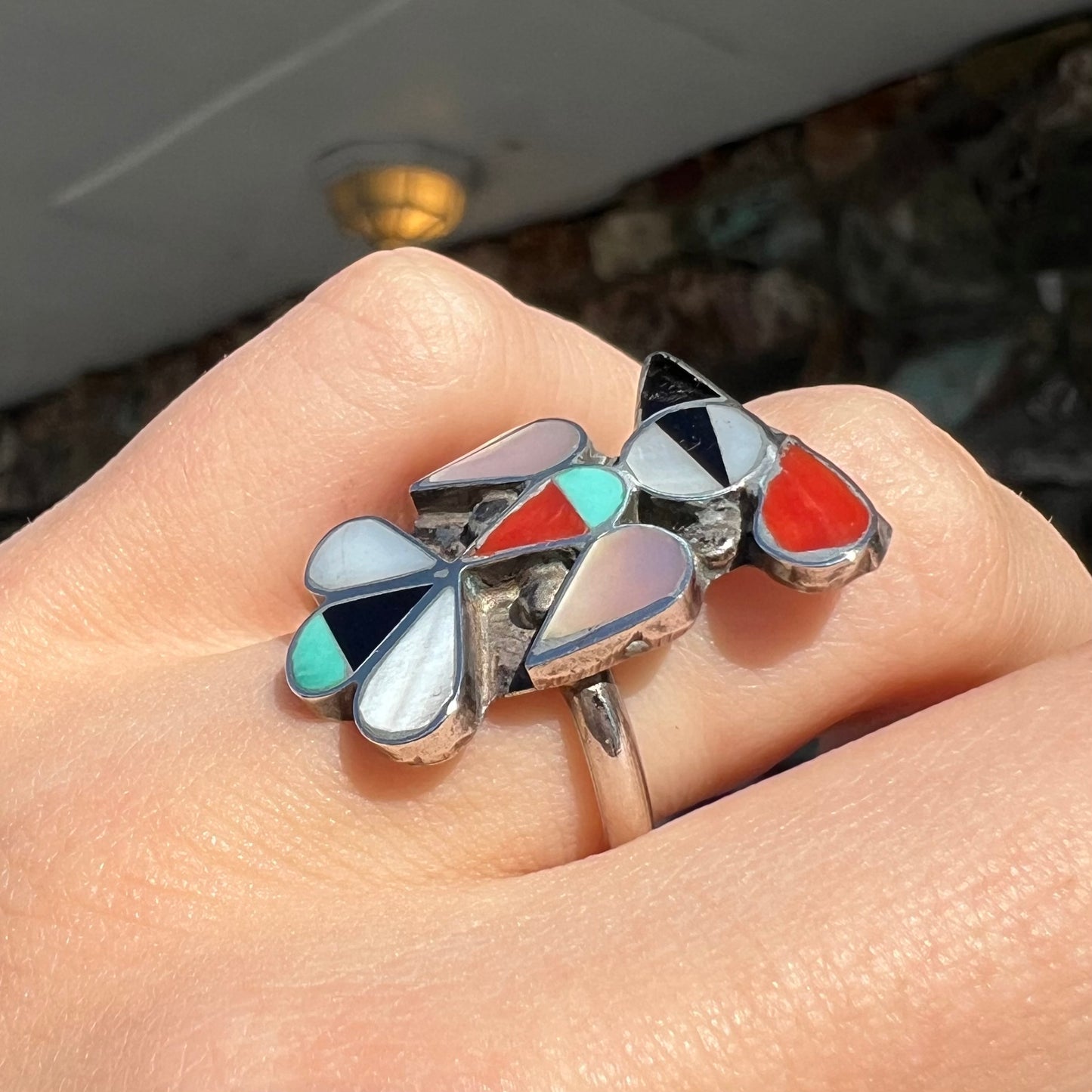 A vintage, sterling silver Zuni thunderbird ring inlaid with turquoise, mother of pearl, onyx, and coral stones.