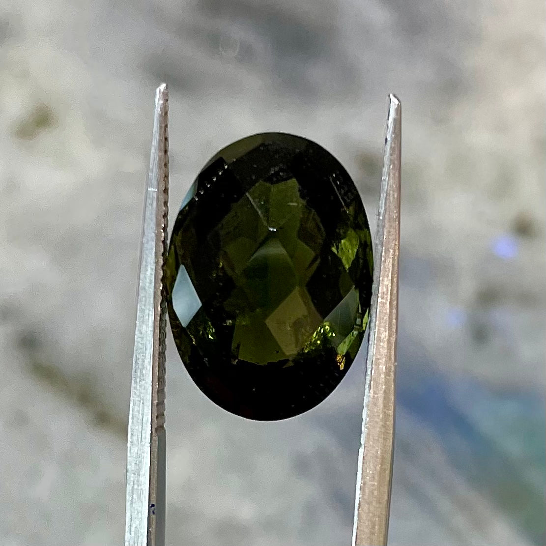 A loose faceted oval checkerboard cut moldavite stone.