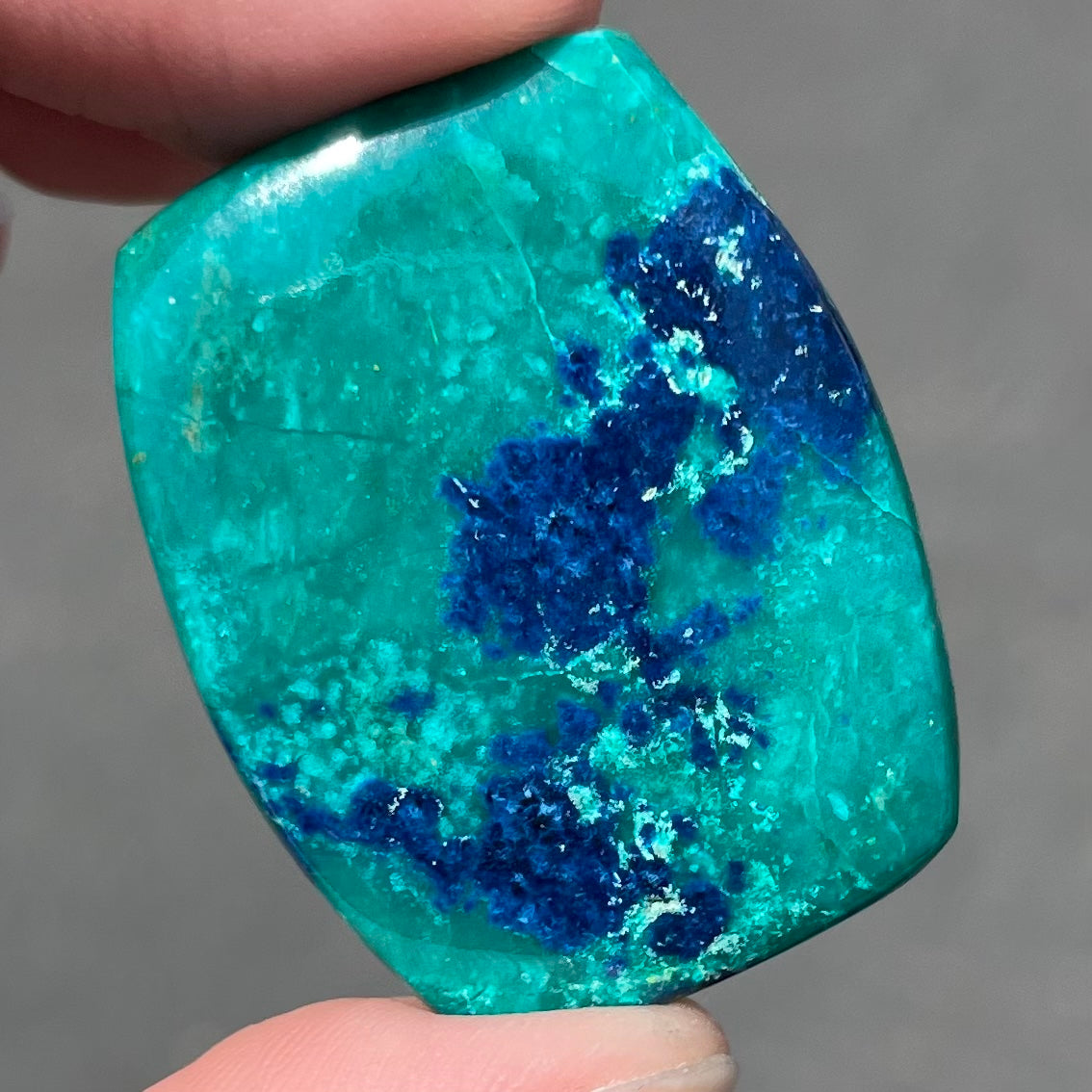 A polished, cushion shaped chrysocolla stone with azurite inclusions.