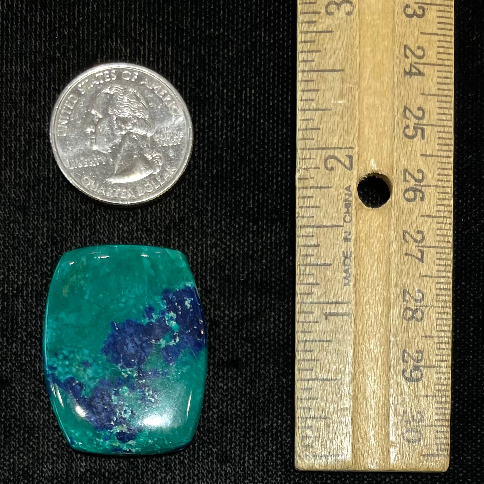 A polished, cushion shaped chrysocolla stone with azurite inclusions.