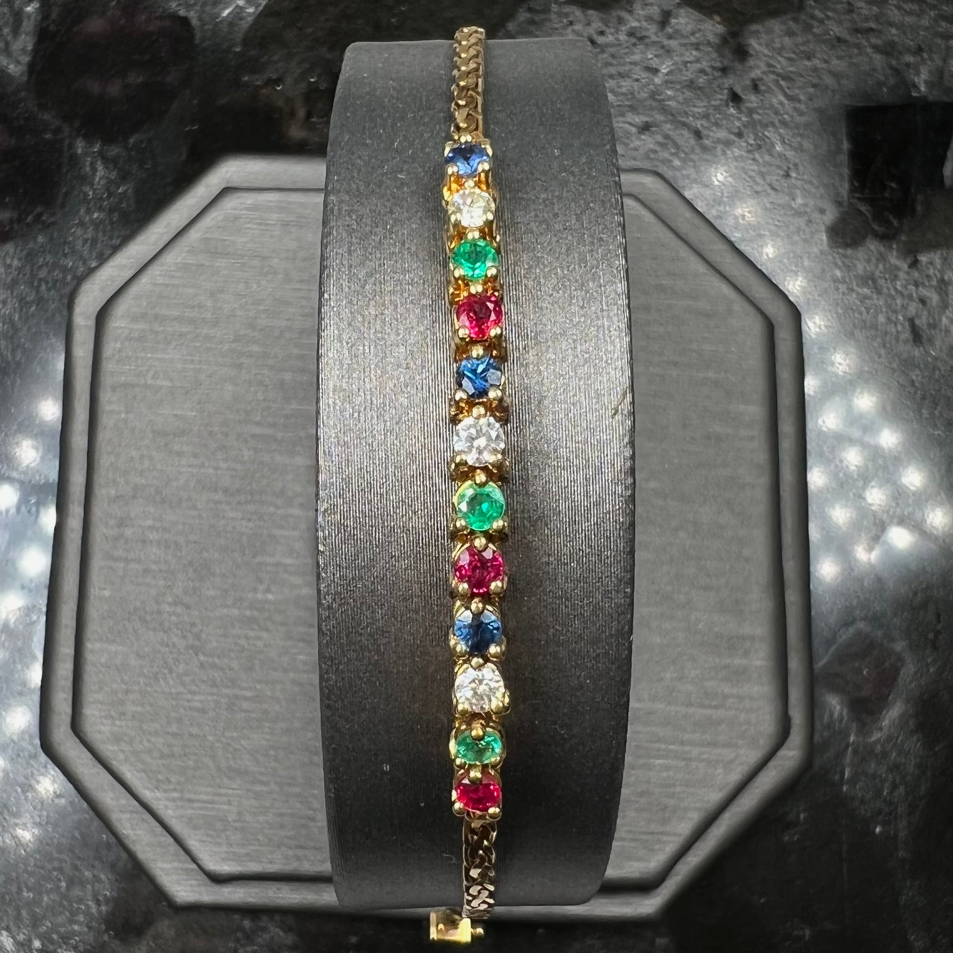 An 18k yellow gold bracelet set with natural rubies, sapphires, diamonds, and emeralds.