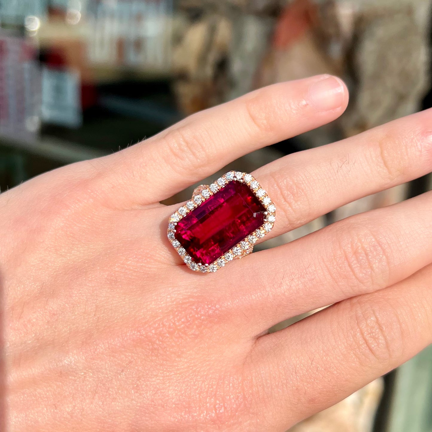 Red emerald cut rubellite tourmaline gemstone set with near flawless round cut diamonds in rose gold.