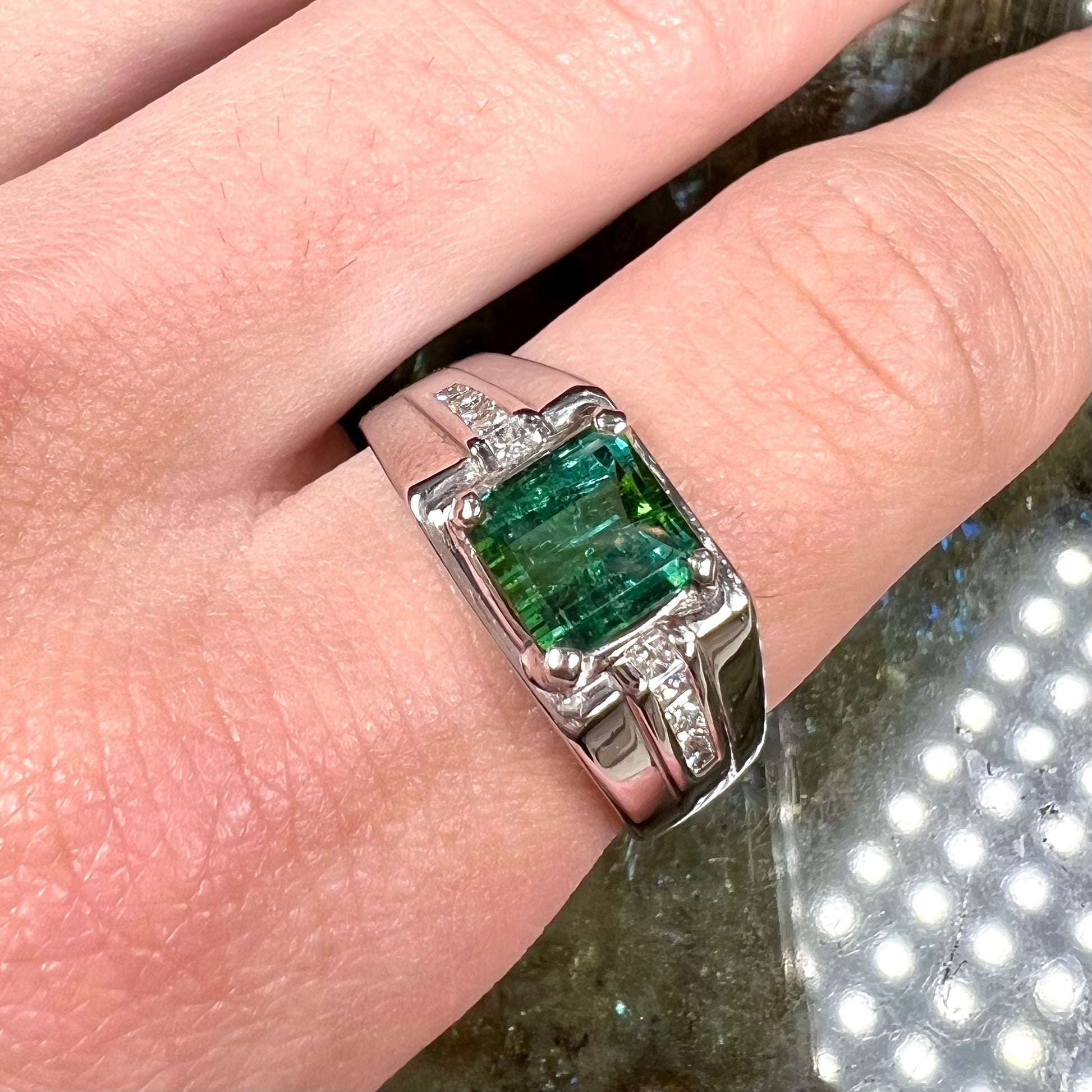 An 18k white gold green tourmaline and diamond men's ring.  The stones are princess cut.