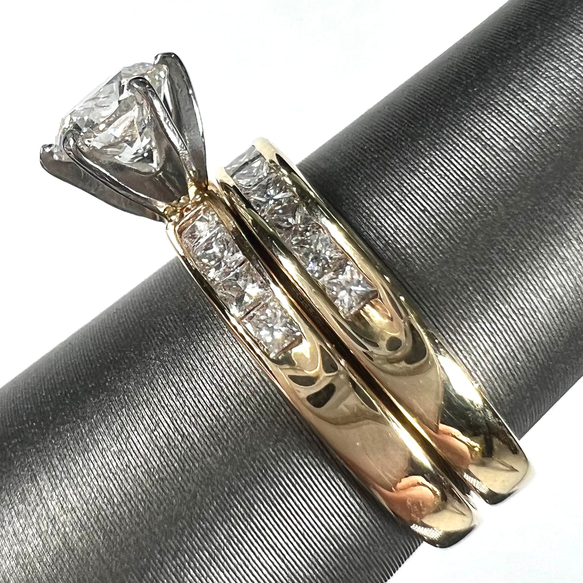 A diamond engagement and wedding ring set.  The center stone is a 1 carat round diamond, and the side stones are channel set princess cut diamonds.