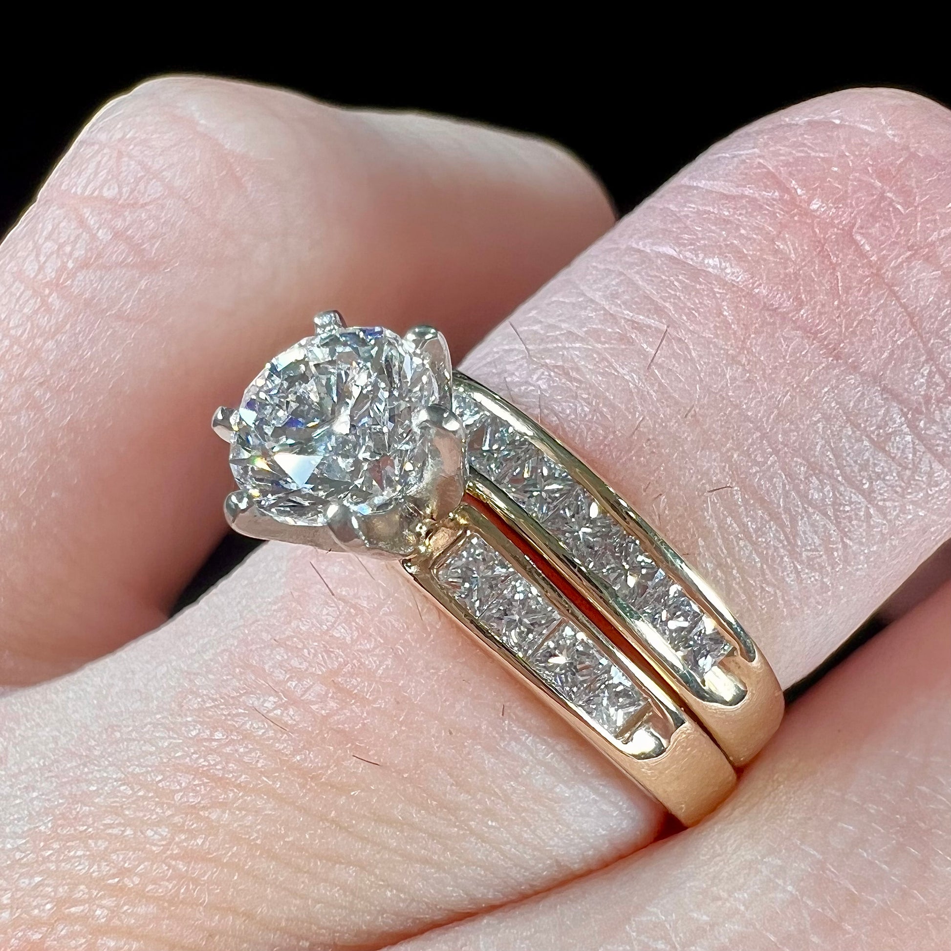 A diamond engagement and wedding ring set.  The center stone is a 1 carat round diamond, and the side stones are channel set princess cut diamonds.