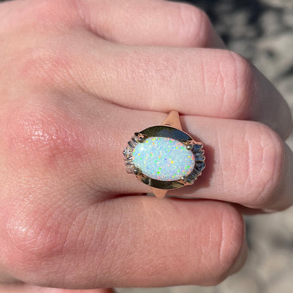 A yellow gold ring set with a synthetic, lab created white opal and two natural diamond accents.