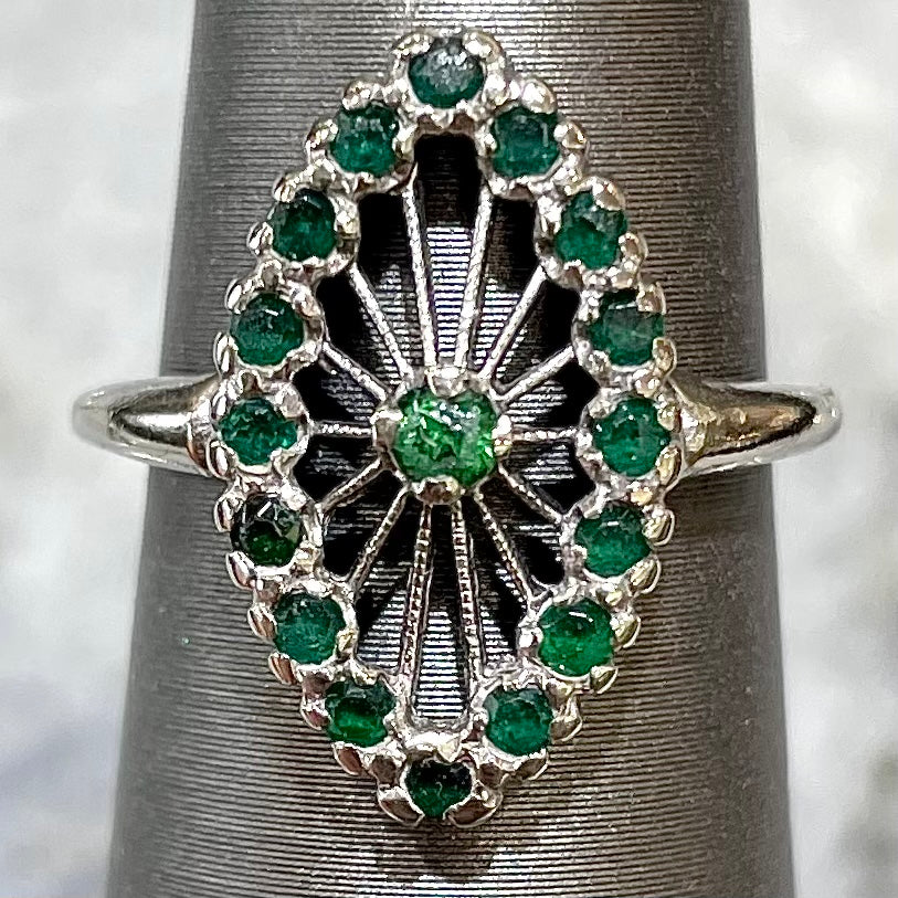 A vintage marquise shape white gold ring set with a halo of round cut emeralds around a single center stone.