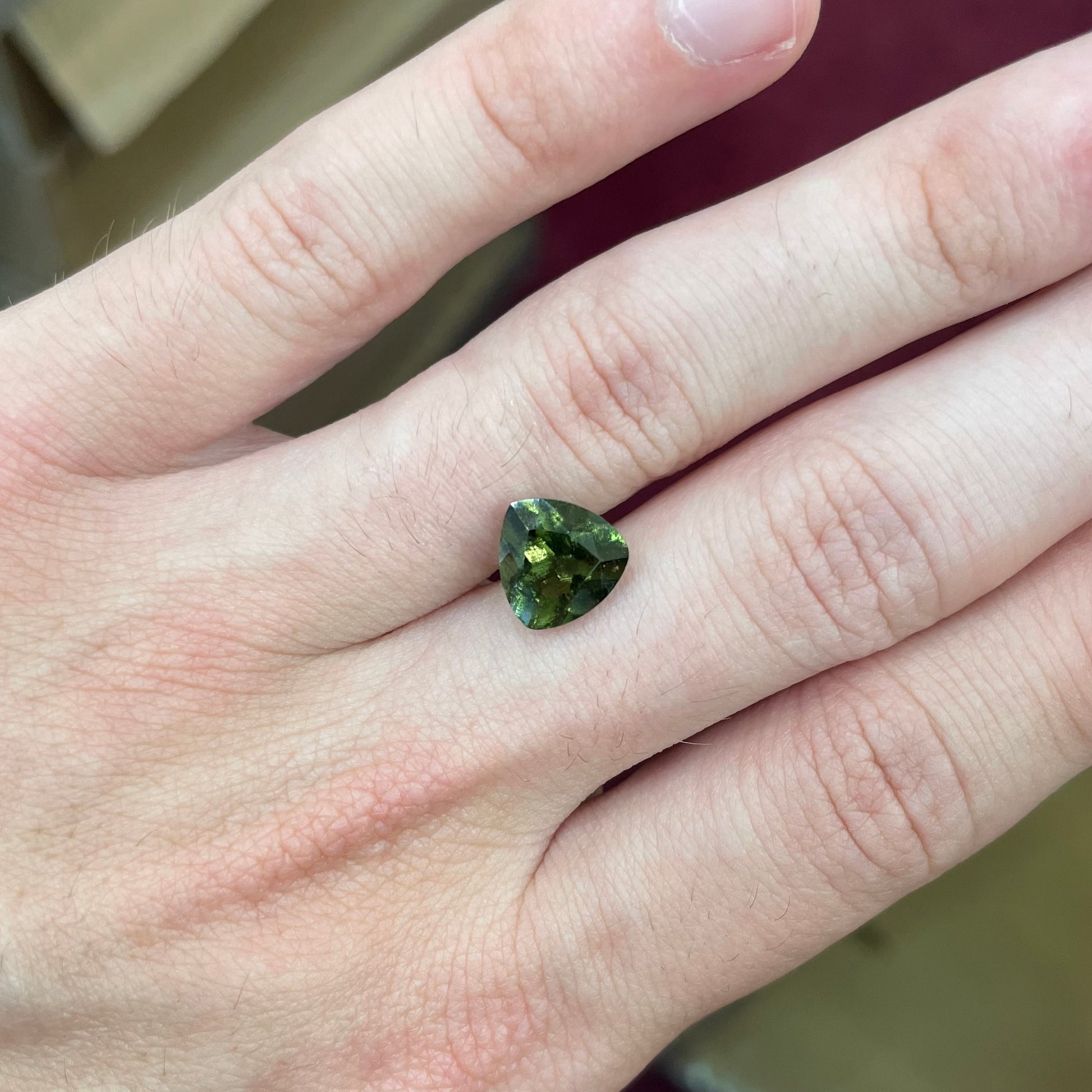A loose, faceted trillion cut moldavite stone that weighs 2.73 carats.