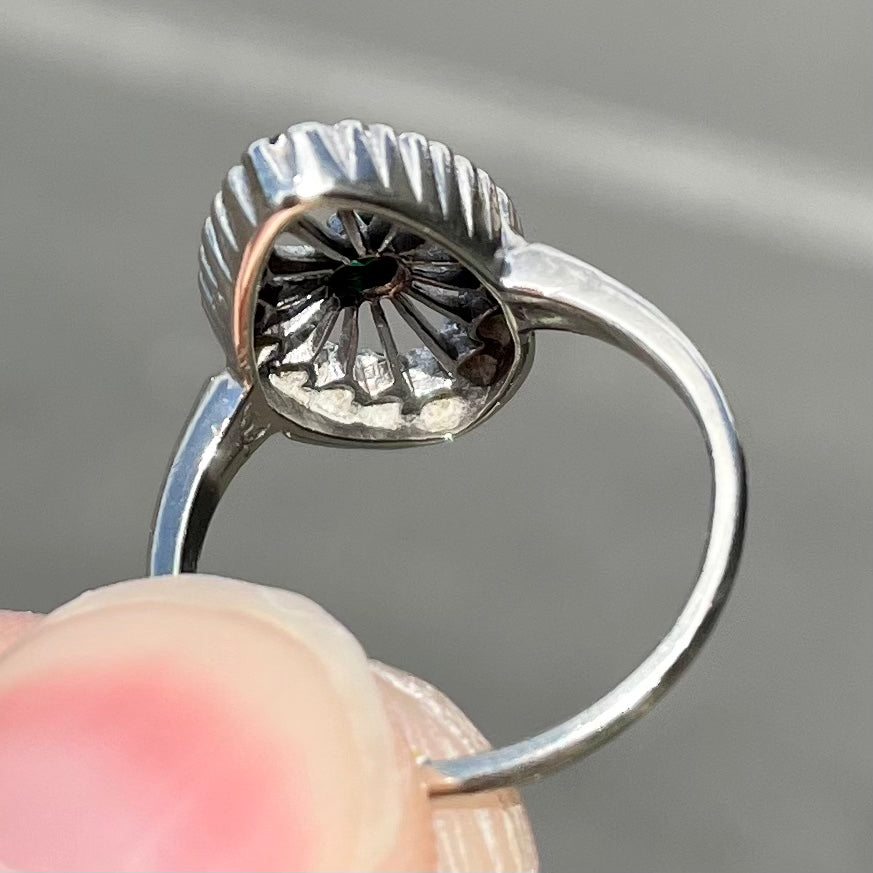 A vintage marquise shape white gold ring set with a halo of round cut emeralds around a single center stone.