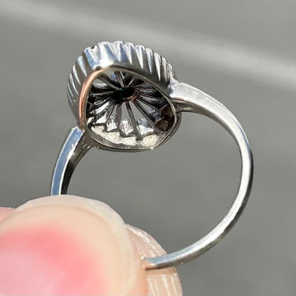 A vintage marquise shape white gold ring set with a halo of round cut emeralds around a single center stone.