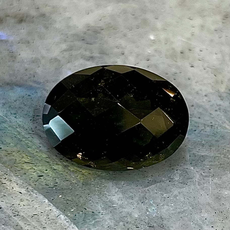 A loose faceted oval checkerboard cut moldavite stone.