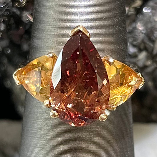 A gold ring set with a pear shape color change garnet between two trillion cut citrine accent stones.