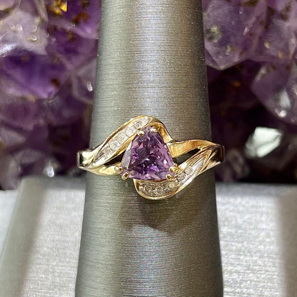 Purple triangle cut amethyst set in a double prong head that covers each corner with channel set clear diamonds in 10kt yellow gold.  Split shank style.