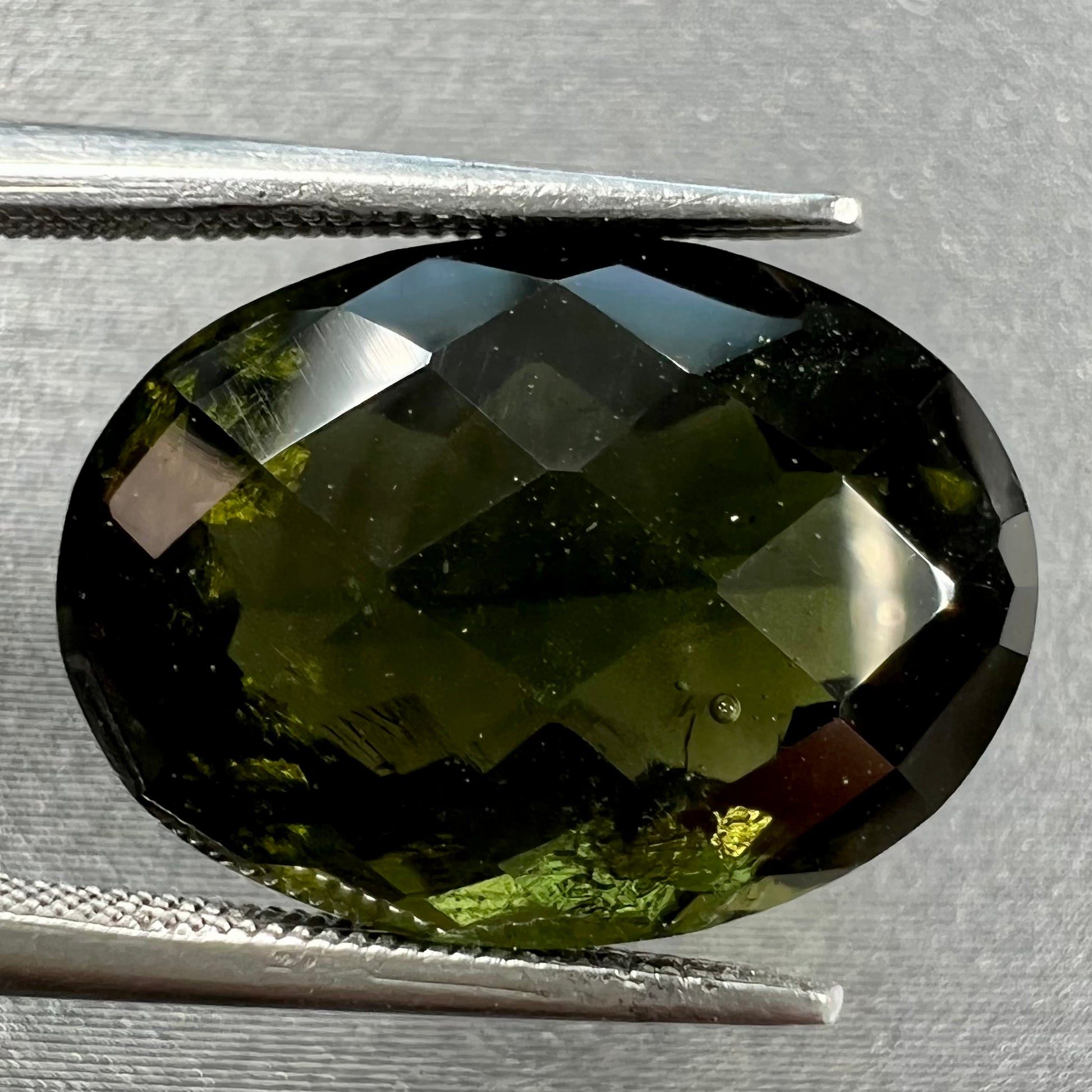 A loose faceted oval checkerboard cut moldavite stone.