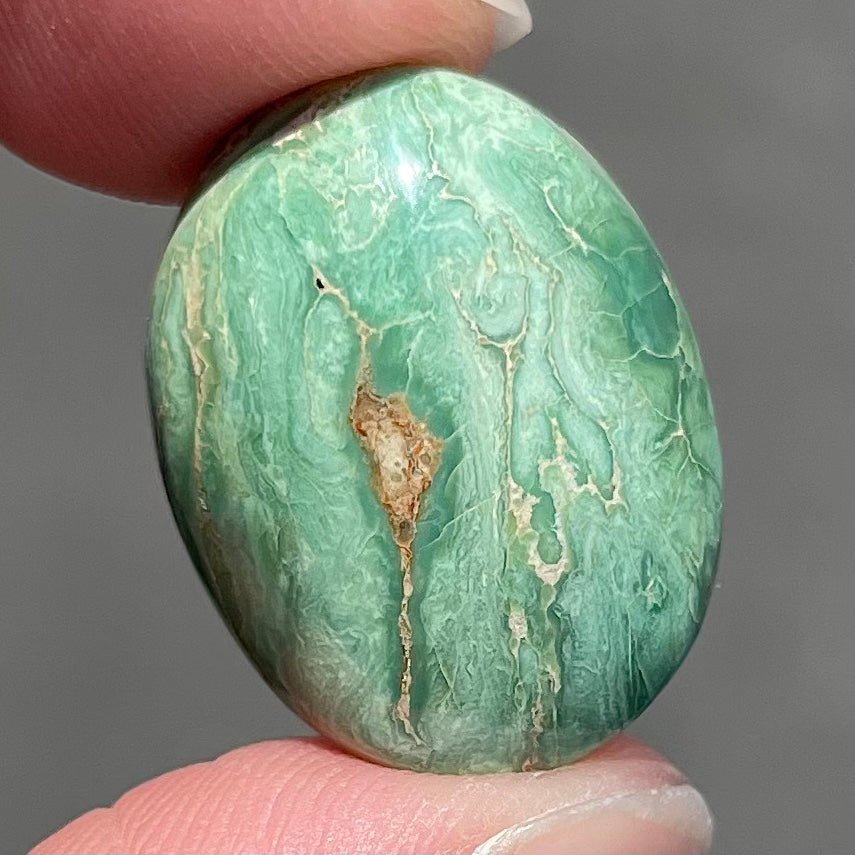A loose, green oval cabochon cut turquoise stone from the Royston Mining District in Nevada.  Green color marbles around a light brown eye.