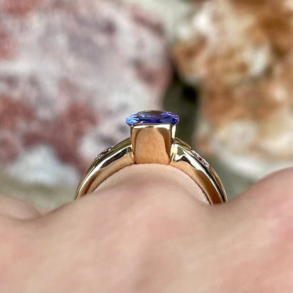 A yellow gold ring half-bezel set with an oval cut blue tanzanite and two flush set round diamonds.