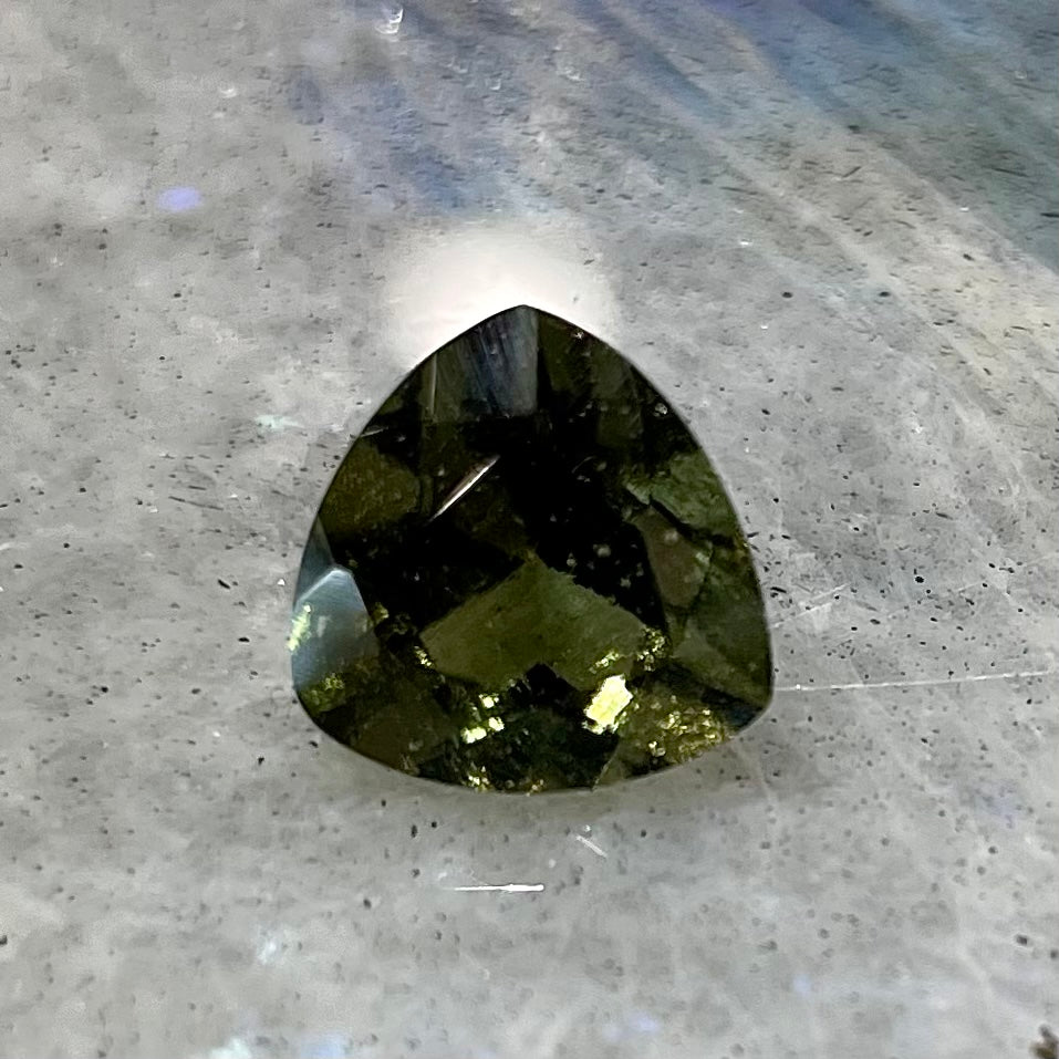A loose, faceted trillion cut moldavite stone that weighs 2.73 carats.