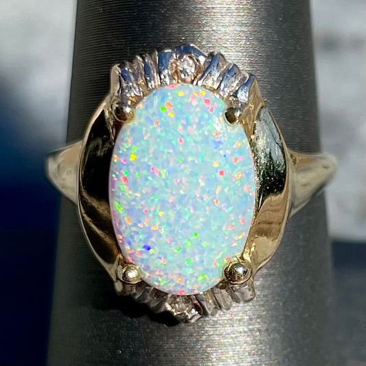 A yellow gold ring set with a synthetic, lab created white opal and two natural diamond accents.