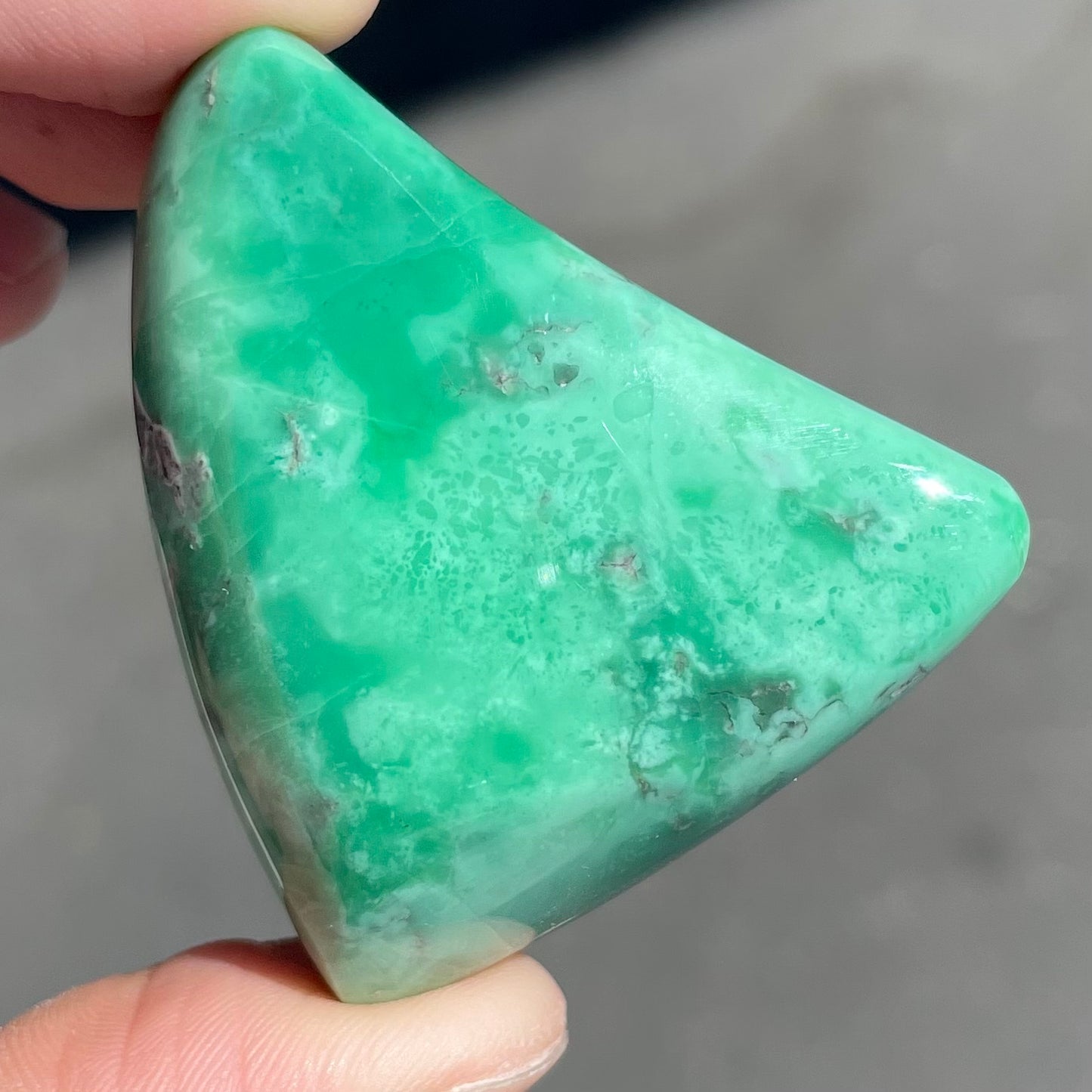 A loose, polished triangular cabochon cut variscite stone from Utah, USA.