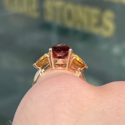 A gold ring set with a pear shape color change garnet between two trillion cut citrine accent stones.