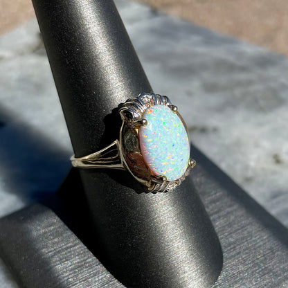 A yellow gold ring set with a synthetic, lab created white opal and two natural diamond accents.