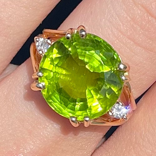 A ladies' round brilliant cut peridot statement ring set with two round diamond accents in yellow gold.