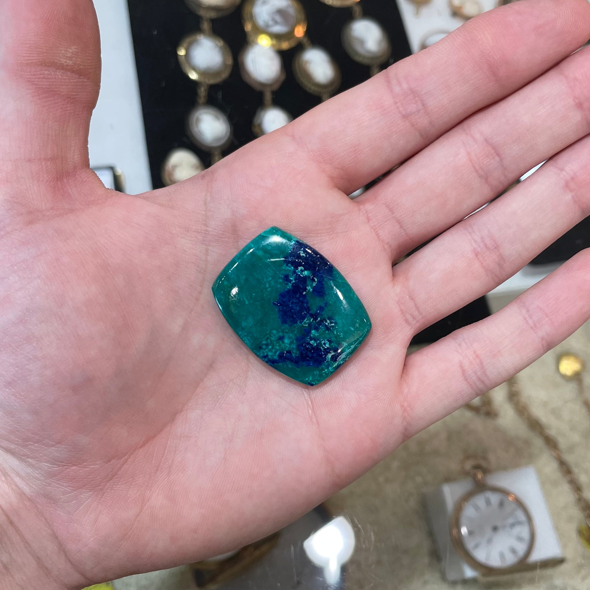 A polished, cushion shaped chrysocolla stone with azurite inclusions.